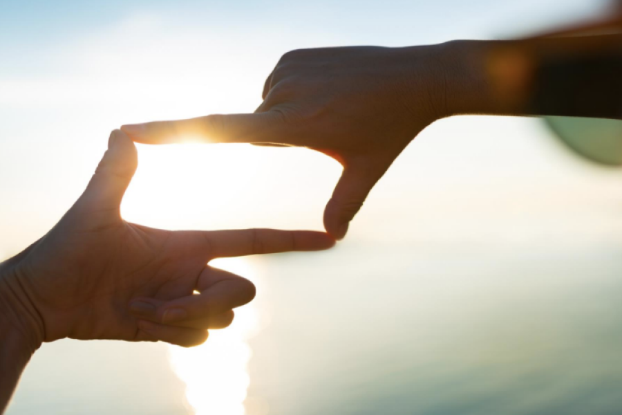 To hender danner en rektangelform som rammer inn sollyset, med hav og himmel i bakgrunnen.