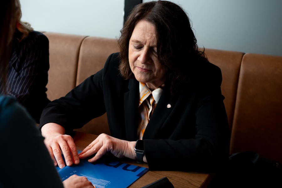 Kvinne med mørkt hår ikledd en sort dressjakke observerer en blå rapport.