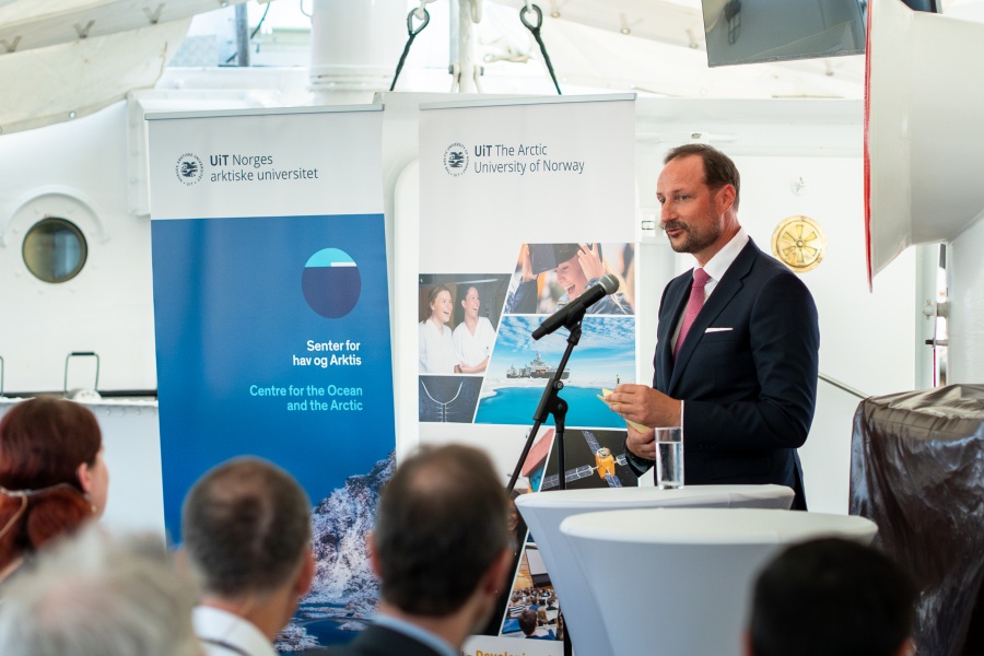En mann i dress holder tale bak et podium med mikrofon under et arrangement. I bakgrunnen står bannere fra UiT Norges arktiske universitet og Senter for hav og Arktis