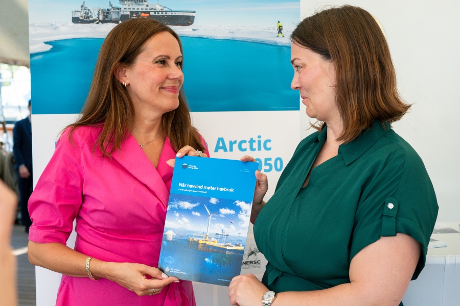 To kvinner holder rapporten mellom seg. Fiskeri- og havministeren ikledd rosa kjole og Sigri Stokke Nilsen ikledd grønn kjole. Begge har brunt hår. 