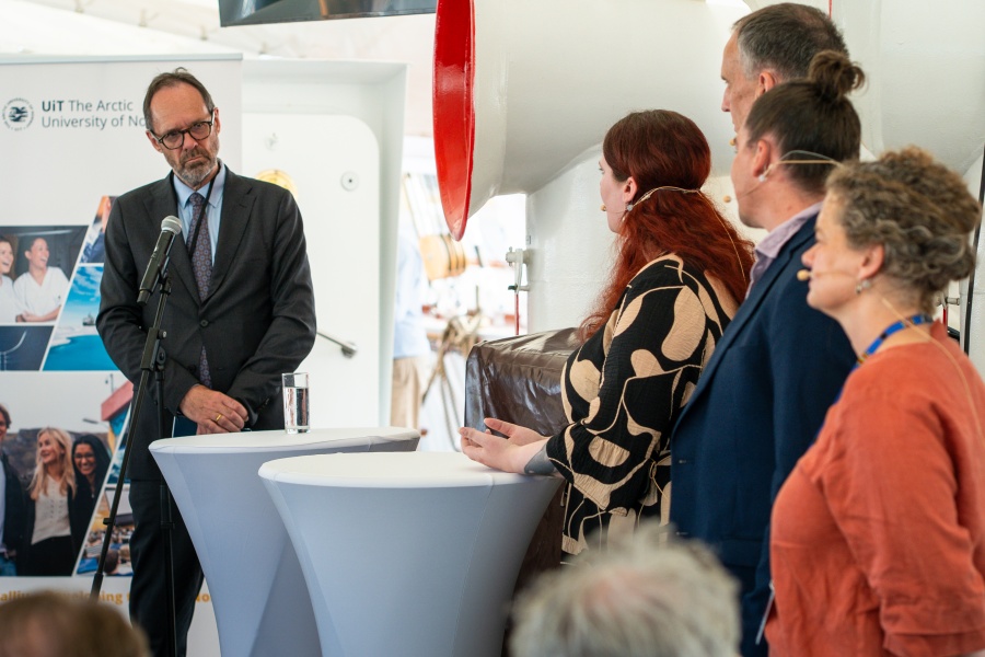 En gruppe personer deltar i en panelsamtale ved høye bord under et arrangement.