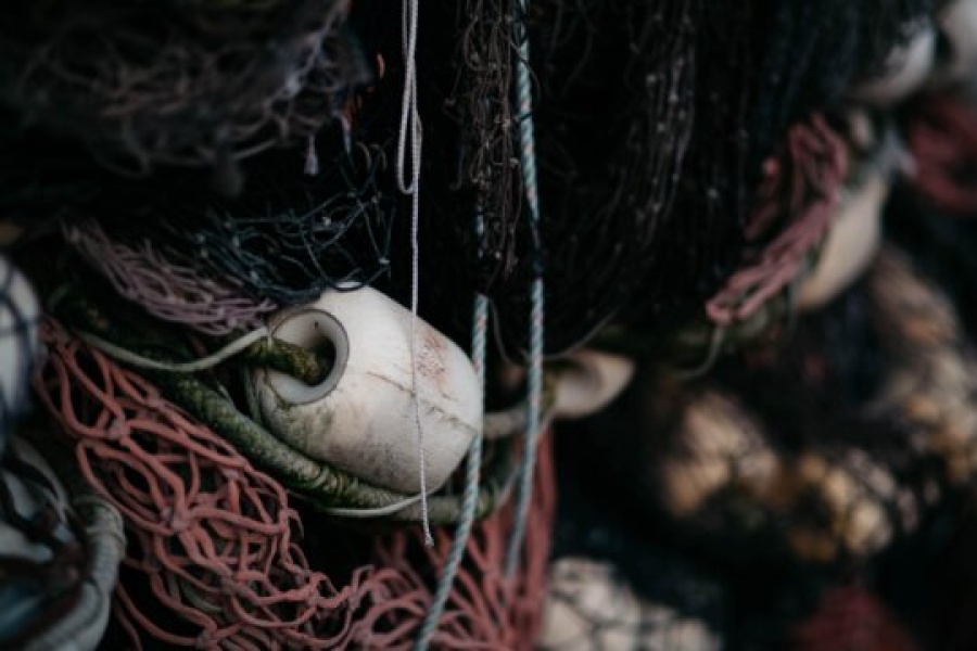Nærbilde av sammenfiltret fiskegarn i ulike farger, med en hvit flytebøye delvis synlig mellom tauene. Teksturen og detaljene i garnet gir et rustikt og autentisk uttrykk.