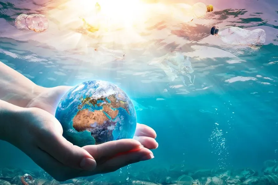 Hender som holder en liten jordklode under vann, omgitt av plastavfall som flyter i havet mens sollyset skinner gjennom vannflaten.