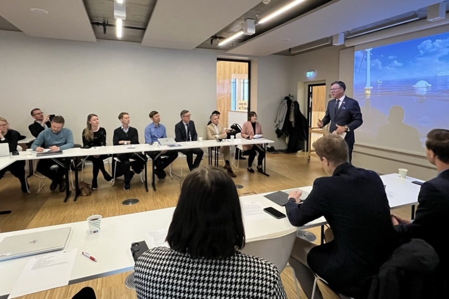 Mennesker samlet i et rom, mens en foredragsholder presenterer foran lerret med bilde av havvindinstallasjoner.