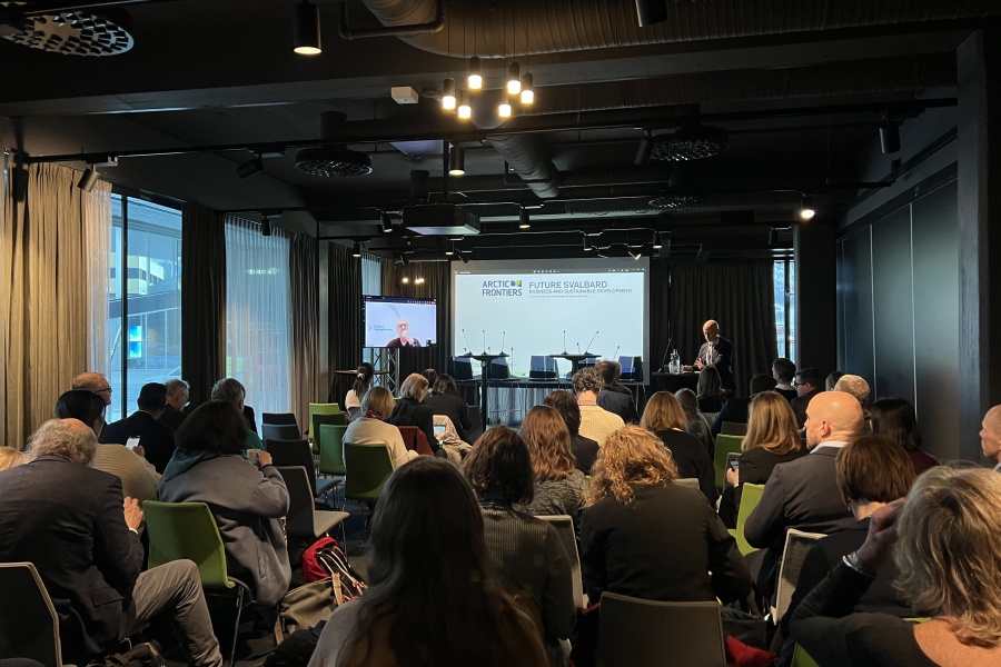 Et konferanserom fylt med deltakere som følger en presentasjon om “Future Svalbard” under Arctic Frontiers, med en taler ved scenen og store vinduer som slipper inn dagslys fra siden.