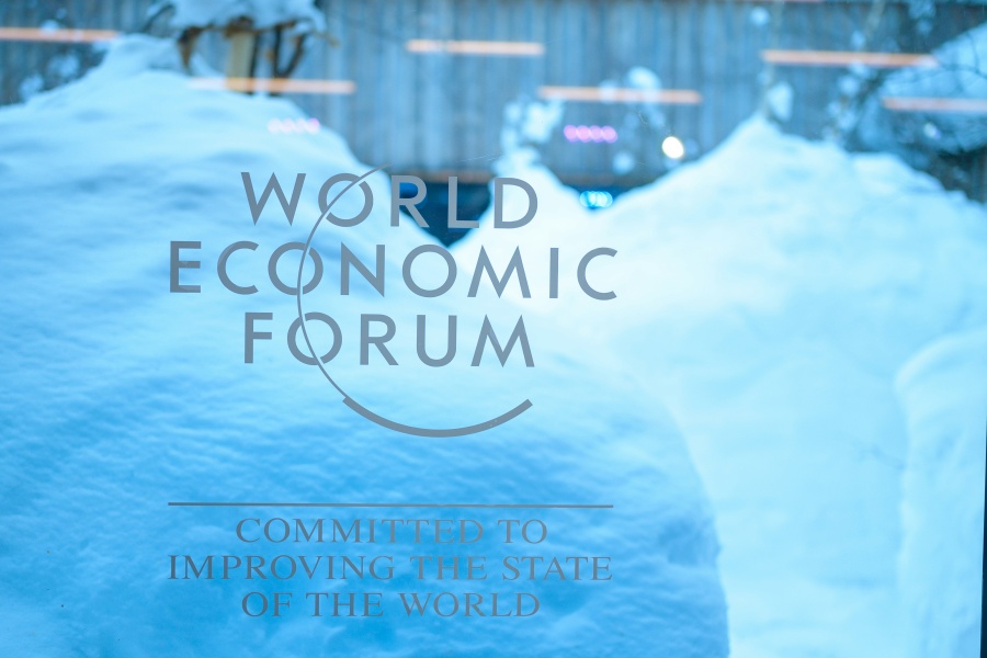 Logoen til World Economic Forum på et vindu, med store snøfonner og et bygg i bakgrunnen. Teksten under logoen lyder «Committed to improving the state of the world».