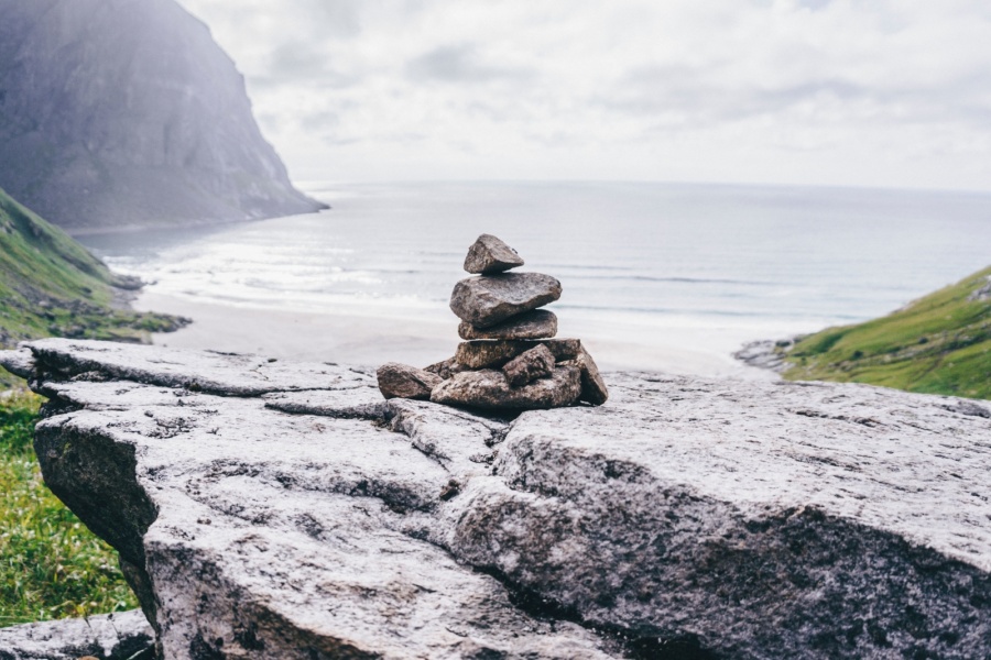 En liten varde av steiner står på en fjellhylle med utsikt mot havet og en strand omgitt av grønne fjellsider.