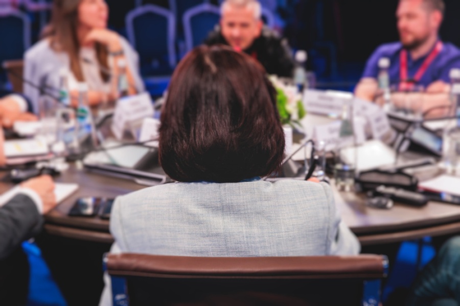 Deltakere i diskusjon rundt et rundt konferansebord, sett bakfra fra en av deltakerne.