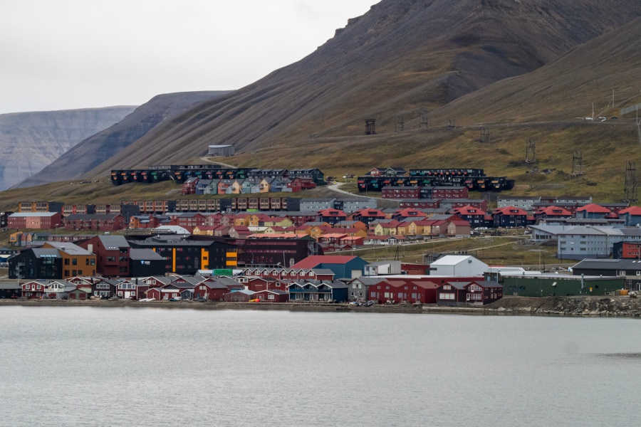 Utsikt over Longyearbyen på Svalbard, med fargerike bygninger langs vannkanten og boligfelt som stiger oppover de bratte, steinete fjellsidene i bakgrunnen.