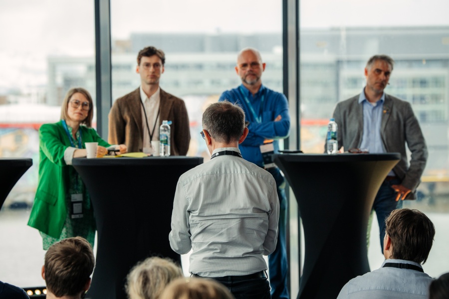 En deltaker stiller spørsmål til et panel under konferanse.