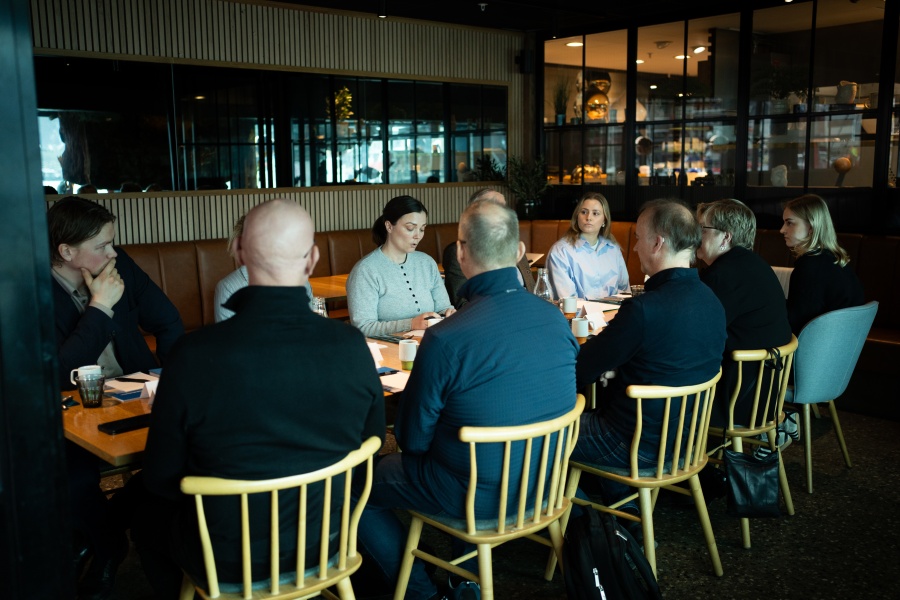 En gruppe personer sitter rundt et bord i et møterom og diskuterer.