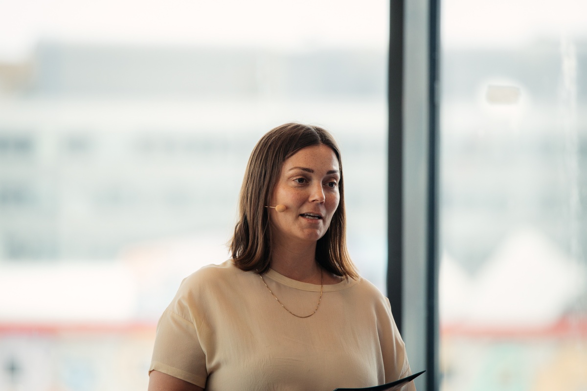 Person med mikrofon holder innlegg foran et vindu.