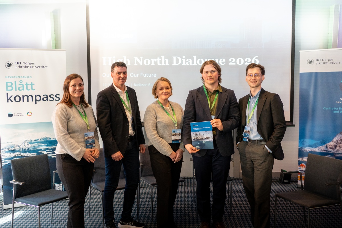 Fem deltakere står sammen på en scene under Havkonferansen «Blått kompass» og High North Dialogue 2026, der én holder en rapport, med bannere fra UiT Norges arktiske universitet i bakgrunnen.