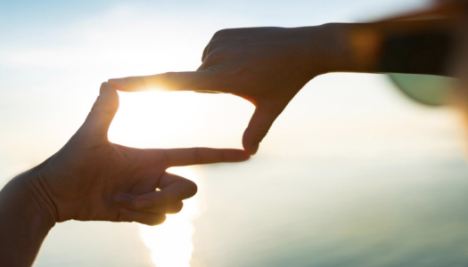 To hender danner en rektangelform som rammer inn sollyset, med hav og himmel i bakgrunnen.