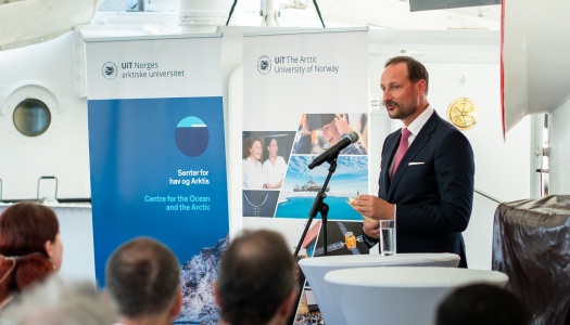 En mann i dress holder tale bak et podium med mikrofon under et arrangement. I bakgrunnen står bannere fra UiT Norges arktiske universitet og Senter for hav og Arktis