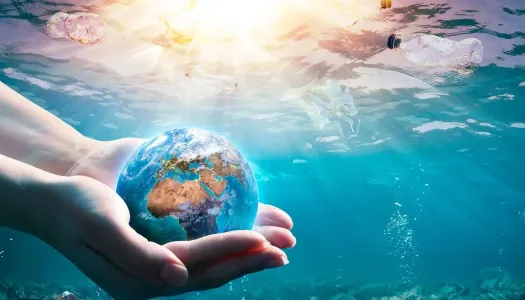 Hender som holder en liten jordklode under vann, omgitt av plastavfall som flyter i havet mens sollyset skinner gjennom vannflaten.