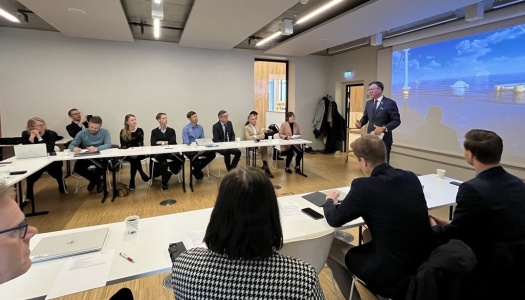 Mennesker samlet i et rom, mens en foredragsholder presenterer foran lerret med bilde av havvindinstallasjoner.