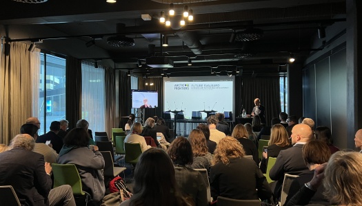 Et konferanserom fylt med deltakere som følger en presentasjon om “Future Svalbard” under Arctic Frontiers, med en taler ved scenen og store vinduer som slipper inn dagslys fra siden.