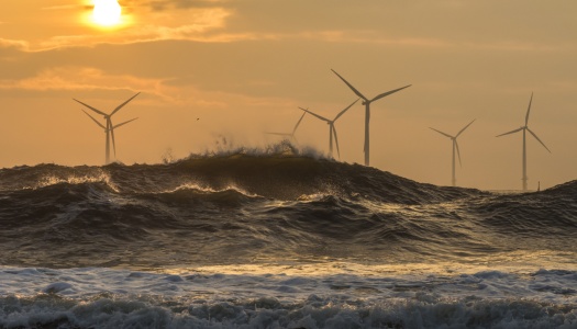 Vindmøller til havs. Bølger i forgrunn, solnedgang i bagkgrunn.