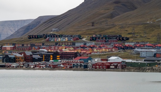 Utsikt over Longyearbyen på Svalbard, med fargerike bygninger langs vannkanten og boligfelt som stiger oppover de bratte, steinete fjellsidene i bakgrunnen.