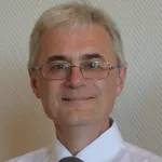 Portrett av mann med hvitt hår og briller som ser rett inn i kamera med et smil. 