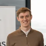 Ung mann smiler foran banner fra UiT Norges arktiske universitet.