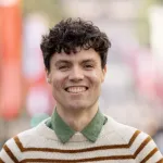 Smilende person med krøllete hår, iført stripet genser, utendørs.