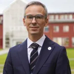 Portrett av mann i dress, stående foran UiTs administrasjonsbygg