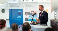 En mann i dress holder tale bak et podium med mikrofon under et arrangement. I bakgrunnen står bannere fra UiT Norges arktiske universitet og Senter for hav og Arktis