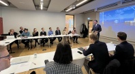 Mennesker samlet i et rom, mens en foredragsholder presenterer foran lerret med bilde av havvindinstallasjoner.