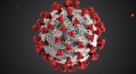 3D illustration of the SARS-CoV-2 virus, showing a spherical gray particle covered with red spike proteins and small orange surface proteins on a dark background.