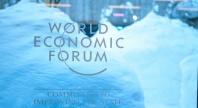 Logoen til World Economic Forum på et vindu, med store snøfonner og et bygg i bakgrunnen. Teksten under logoen lyder «Committed to improving the state of the world».