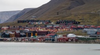 Utsikt over Longyearbyen på Svalbard, med fargerike bygninger langs vannkanten og boligfelt som stiger oppover de bratte, steinete fjellsidene i bakgrunnen.
