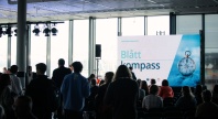 Publikum i en sal. En skjerm med et bilde som sier "Blått kompass"