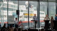 Paneldebatt på konferansen Blått kompass, med flere deltakere på scene foran store vinduer med et Hurtigruten-skip i bakgrunnen.