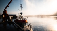 Båt ligger til kai i en liten havn i lavt sollys.