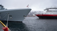 Grått marinefartøy og Hurtigruteskipet Otto Sverdrup ligger ved kai i Tromsø, med snødekte fjell i bakgrunnen.
